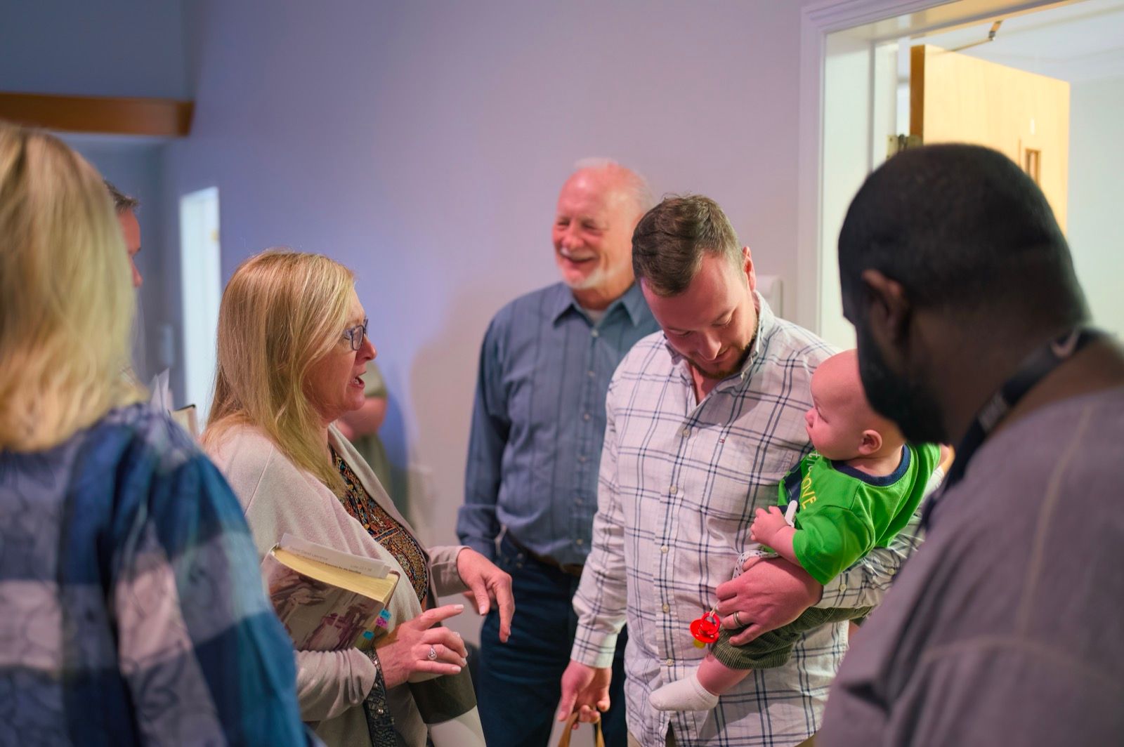 Members of different backgrounds greeting one another before the service, one holding a young child, at Lucy Baptist Church.