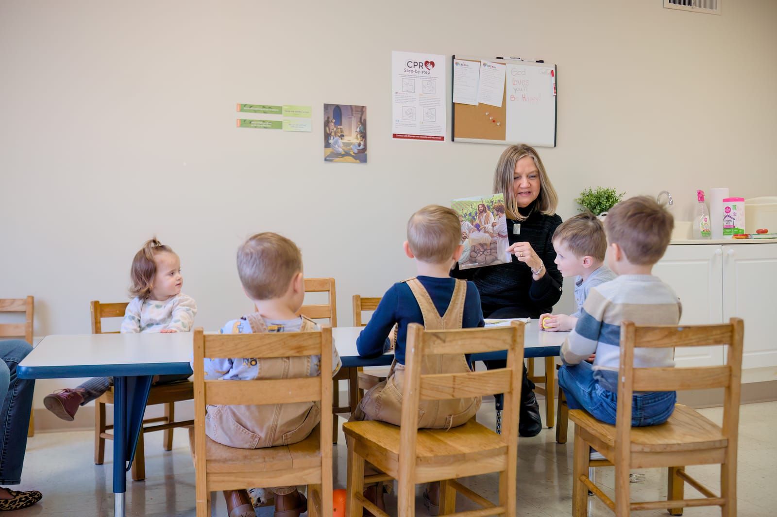 A teacher reading a Bible story to a group of young children seated around a table.